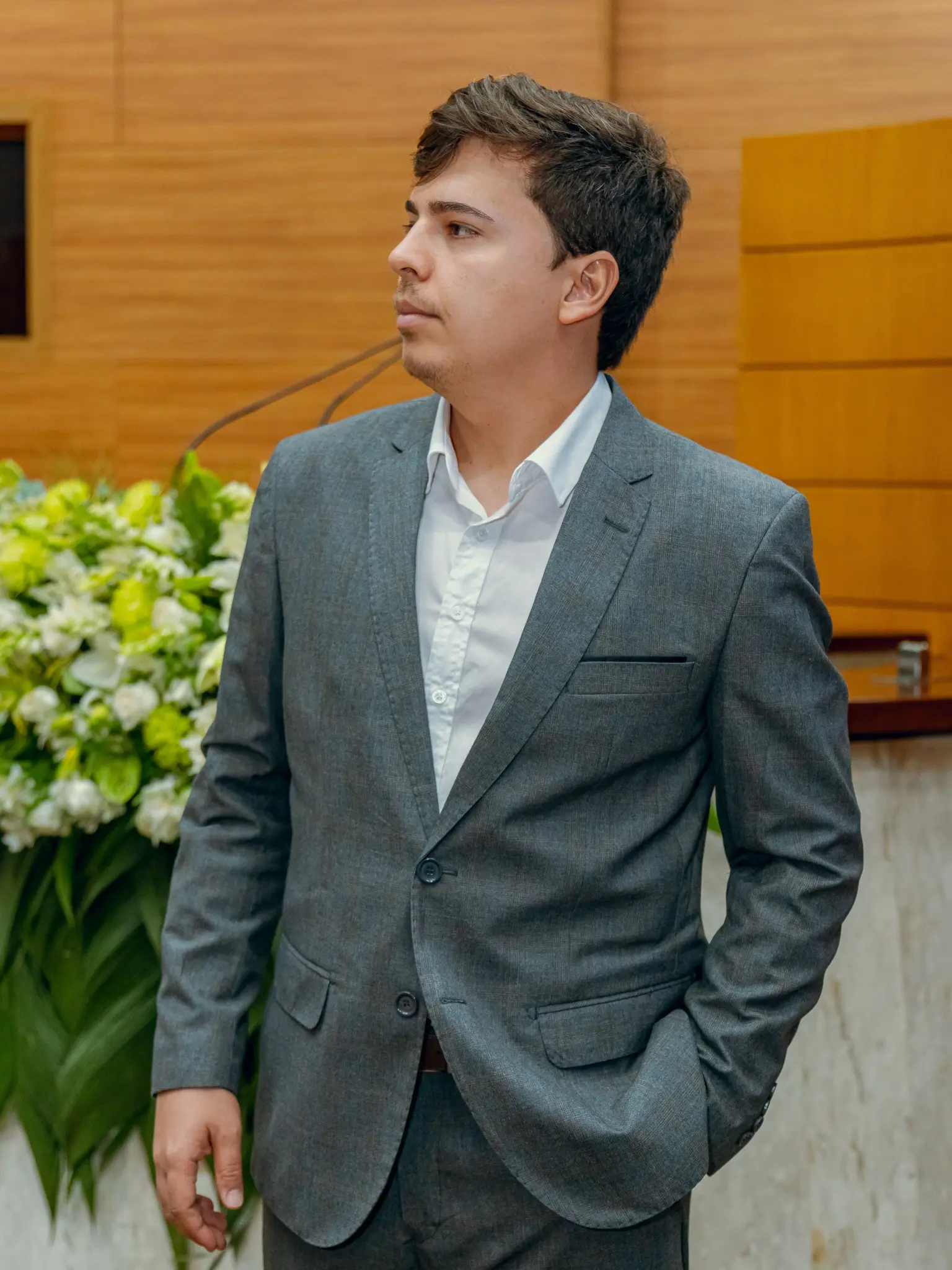 Luciano Moraes vestindo terno cinza em ambiente institucional